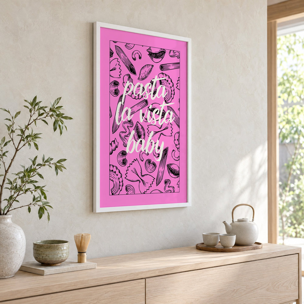 Pasta la vista baby pink print in a white frame above a pale wood console with a matcha tea set