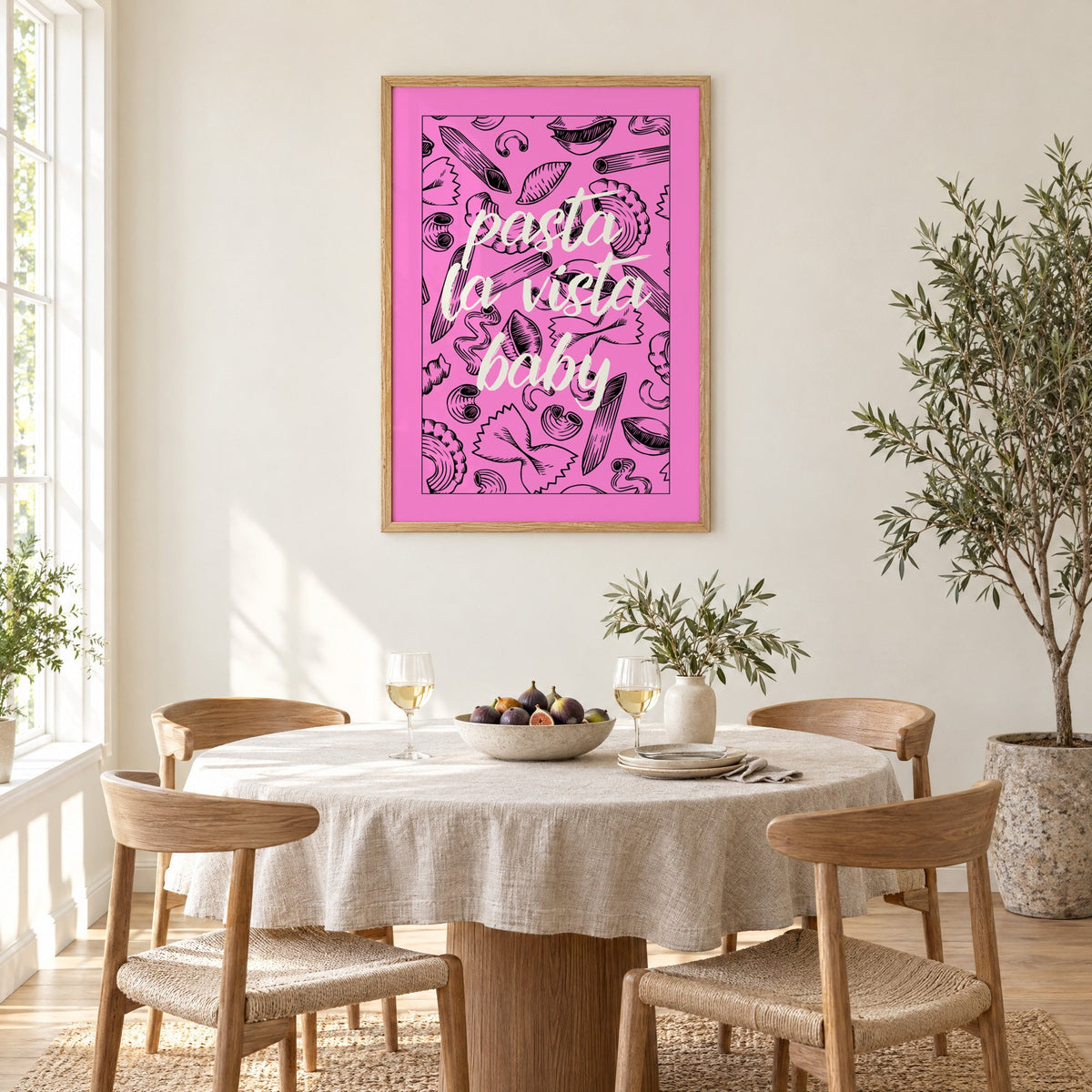 Pasta la vista baby pink print in an oak frame above a round linen-covered dining table with figs and wine
