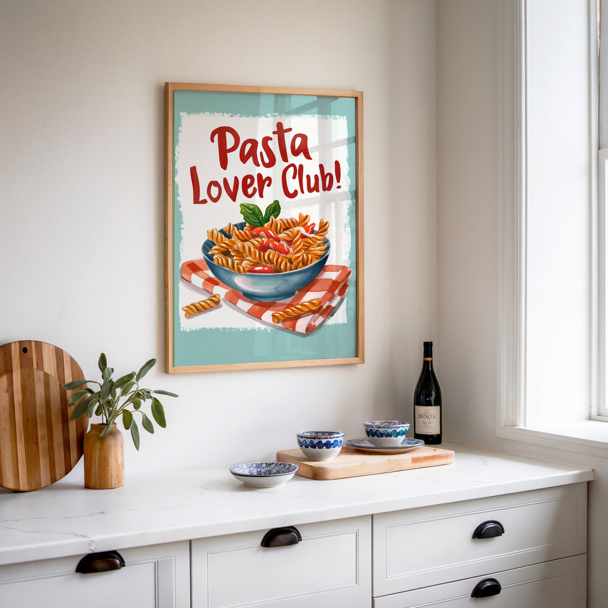 Pasta Lover Club fusilli print in an oak frame above a white sideboard with a bottle of wine