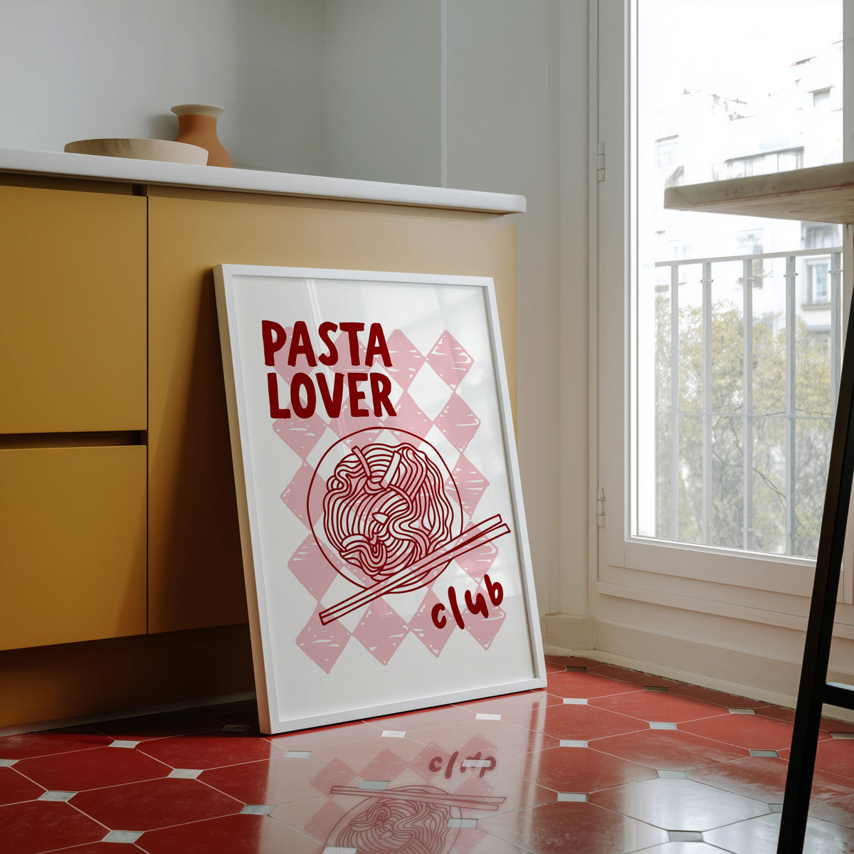 Pasta Lover Club print in a white frame against yellow cabinets on a red tiled floor