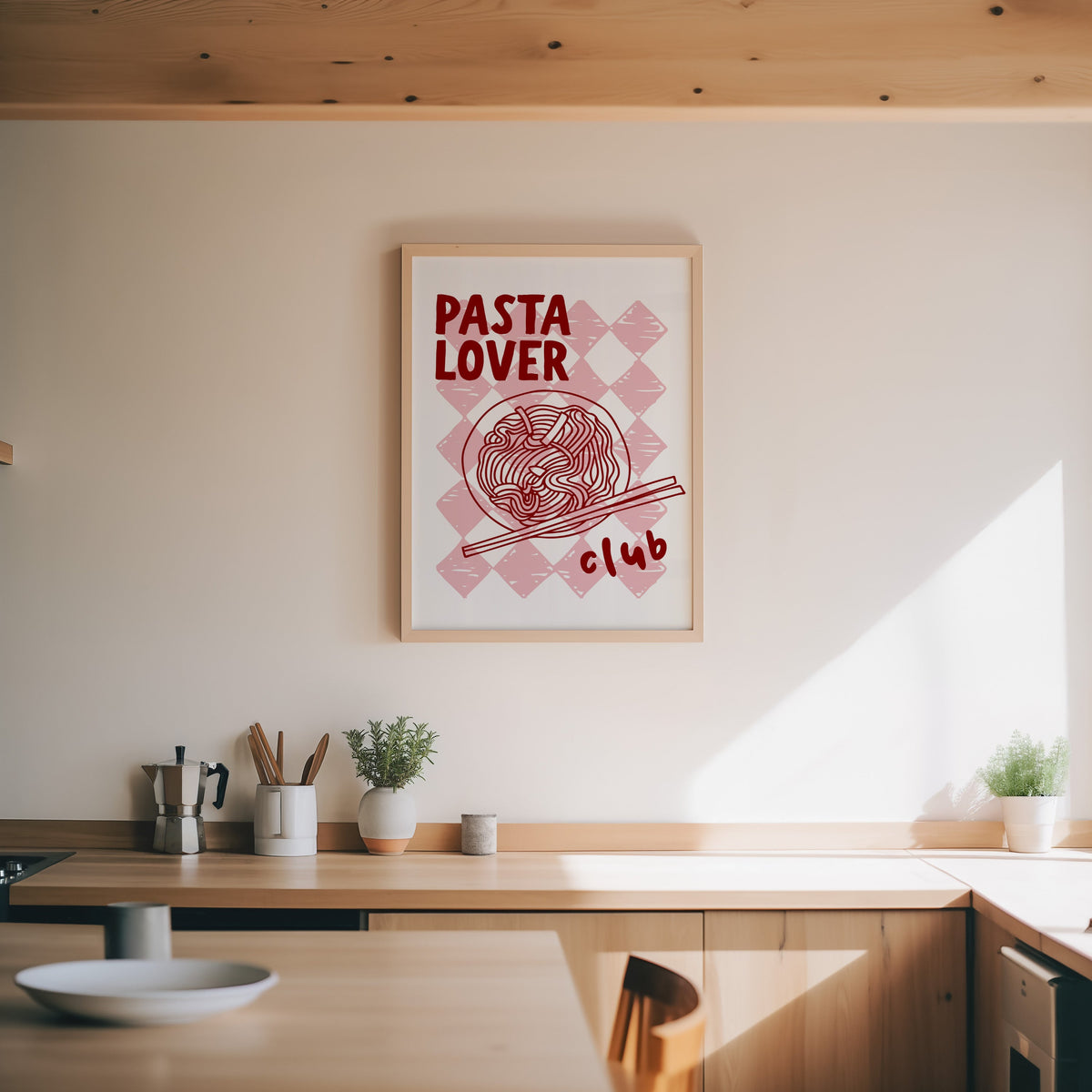 Pasta Lover Club print in an oak frame above a wood counter with a moka pot and herbs