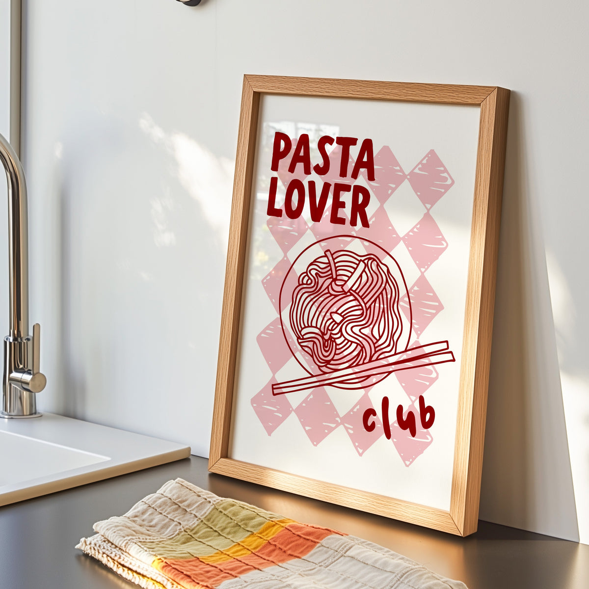 Pasta Lover Club print in an oak frame by the kitchen sink beside a striped tea towel