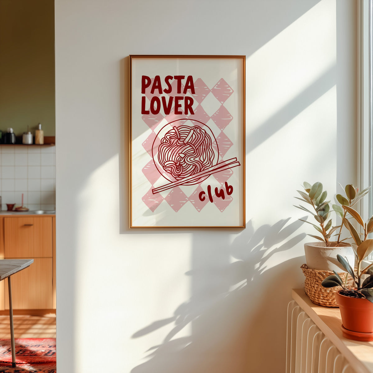 Pasta Lover Club print shown in a gold frame in sunlight with plants and a kitchen beyond