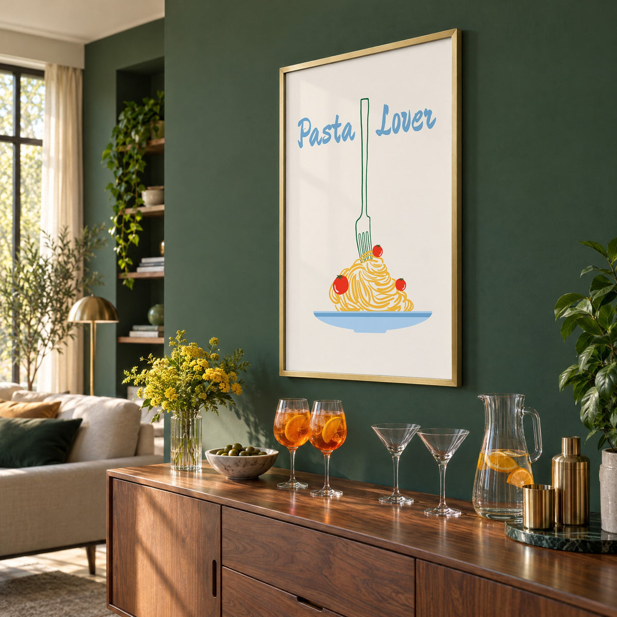 Pasta Lover fork and spaghetti print in a brass frame on a bottle green wall above a sideboard with spritz and martini glasses, seen at an angle