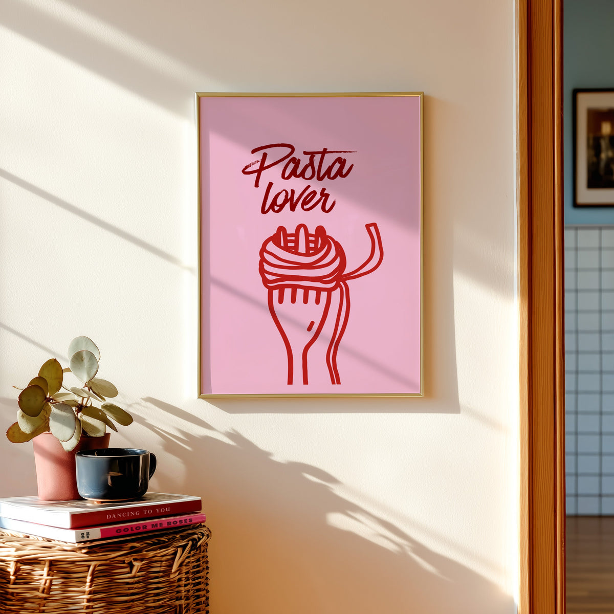 Pasta Lover print in a gold frame above a basket of books and a pilea plant