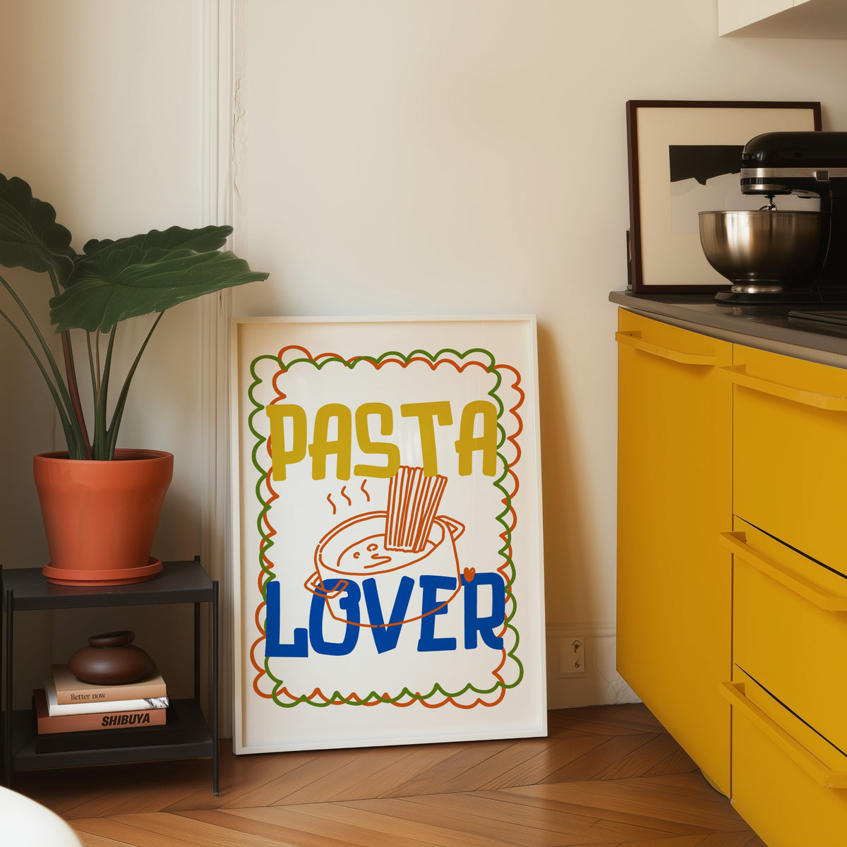 Pasta Lover print in a white frame leaning on parquet beside a bright yellow kitchen