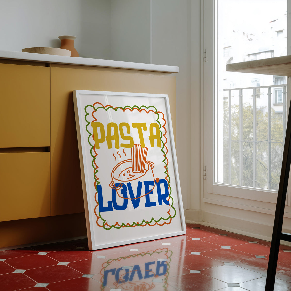 Pasta Lover print in a white frame against yellow cabinets on a red tiled floor