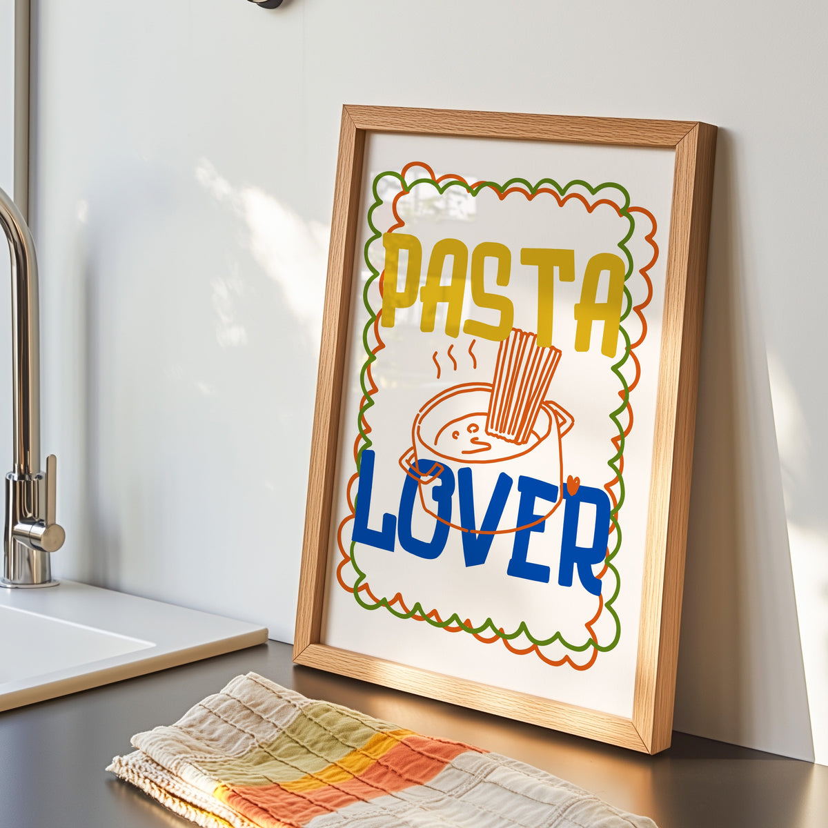 Pasta Lover print in an oak frame by the kitchen sink beside a striped tea towel
