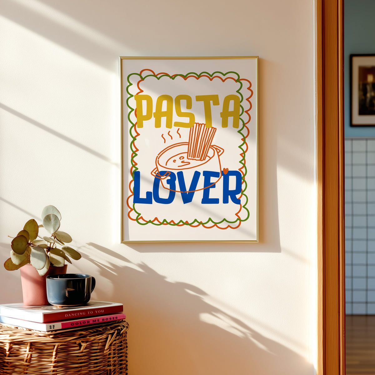 Pasta Lover print shown in a gold frame above a basket of books and a pilea plant