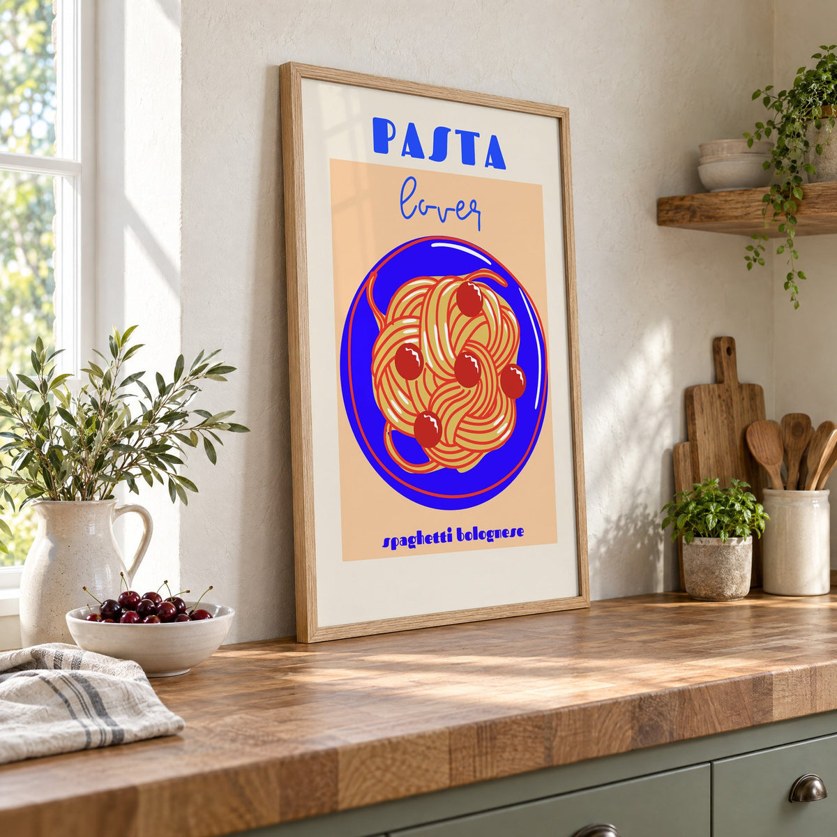 Pasta lover blue plate spaghetti print in an oak frame leaning on a butcher block island beside a bowl of cherries