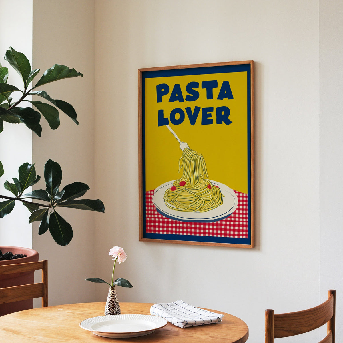 Pasta Lover yellow print in a walnut frame above a round table beside a fiddle-leaf fig