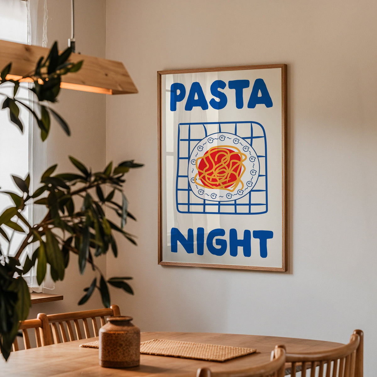 Pasta night blue print in a walnut frame above a dining table beside an olive tree