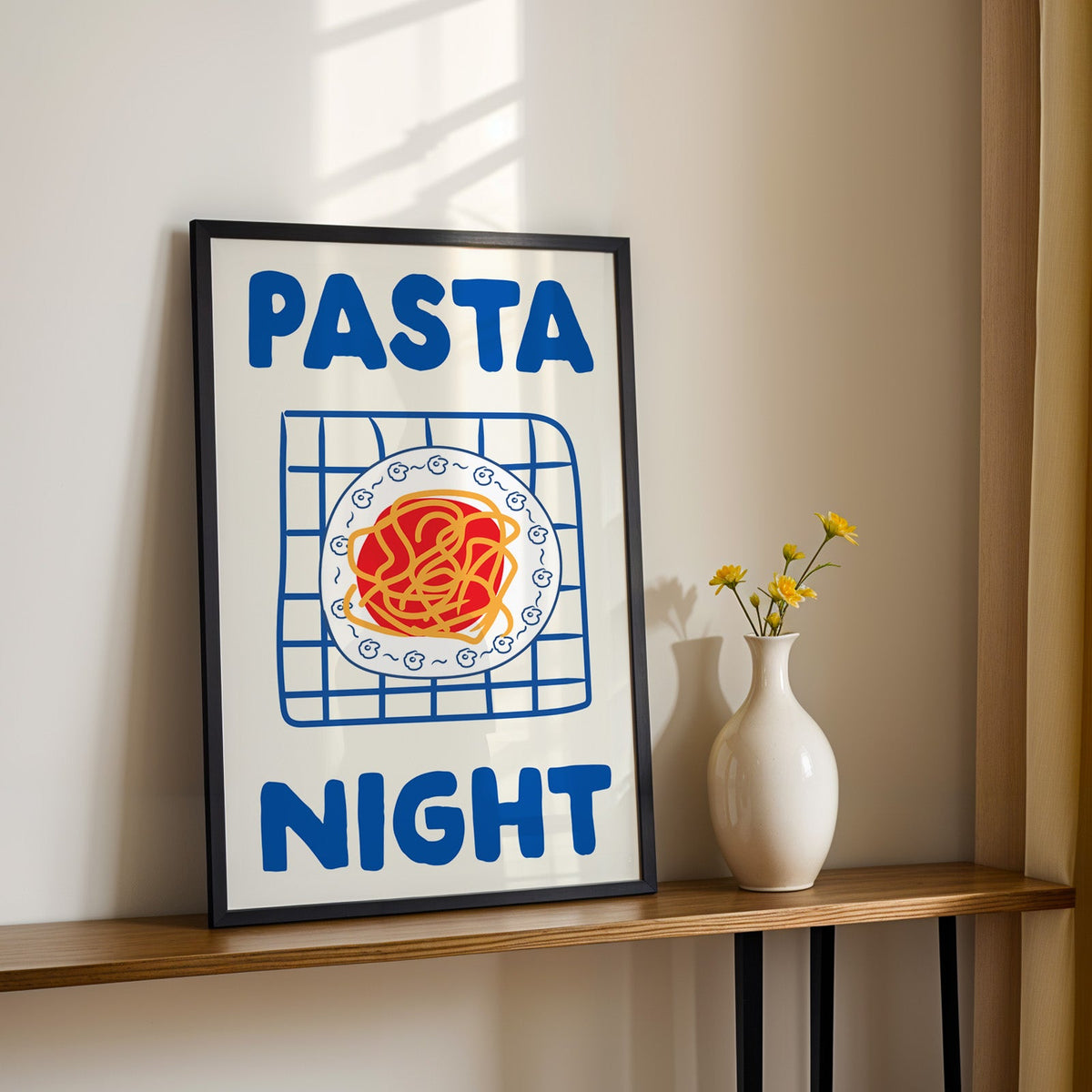 Pasta night blue print in a black frame on a console table with yellow daisies