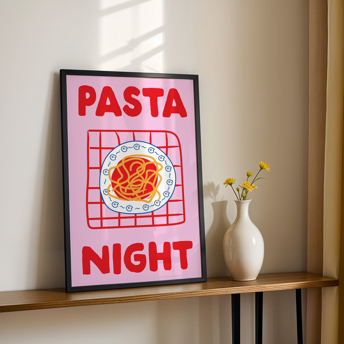 Pasta night pink print in a black frame on a console table with yellow daisies