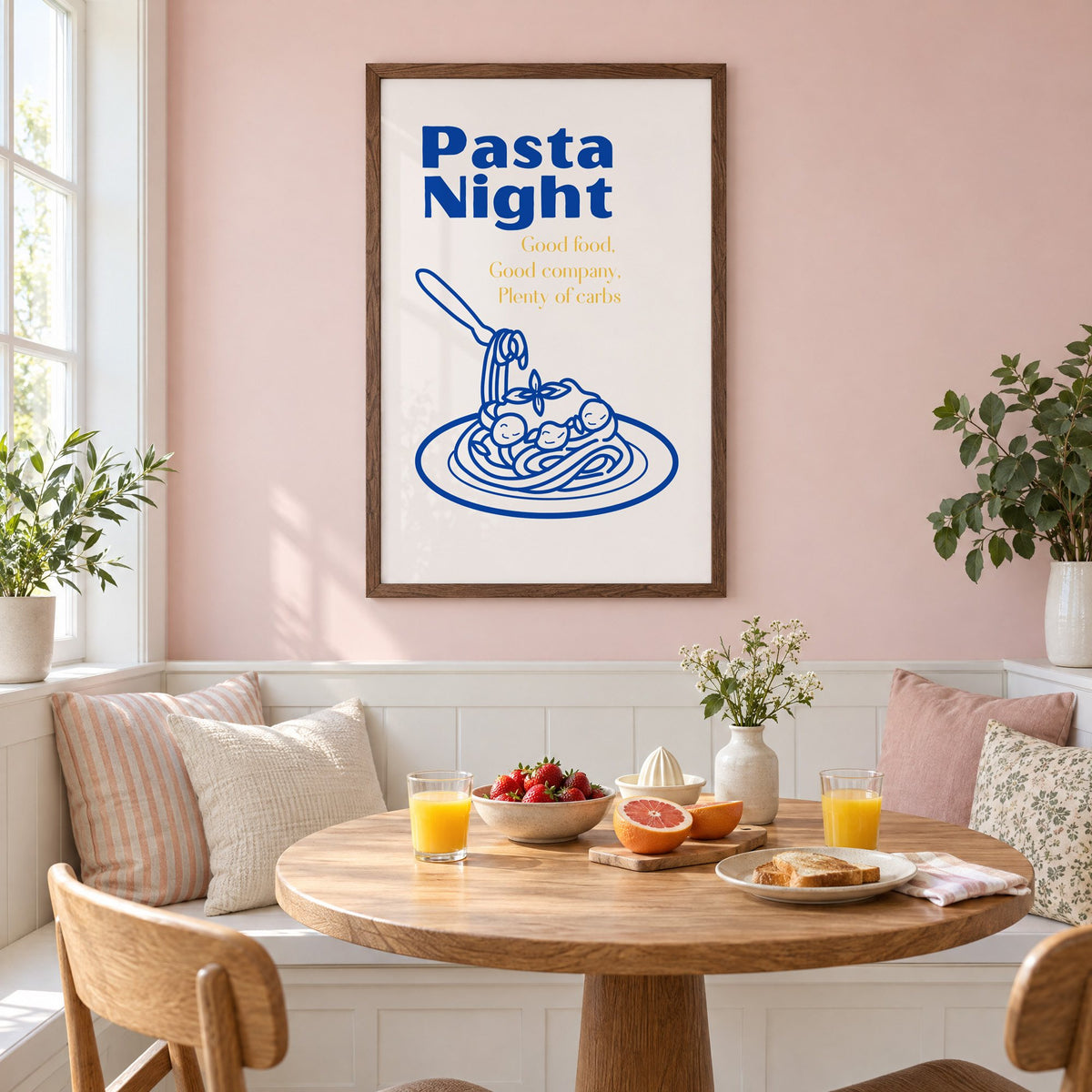Pasta Night cobalt spaghetti and meatballs print in a walnut frame on a pastel pink wall above a breakfast nook with strawberries and orange juice