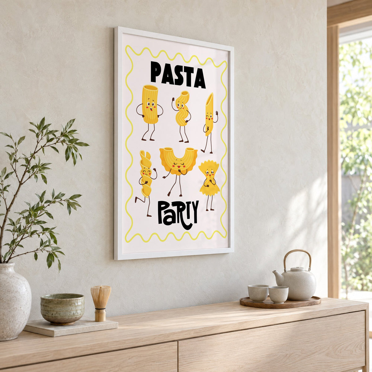 Pasta Party cartoon noodles print in a white frame above a pale wood console with a matcha tea set