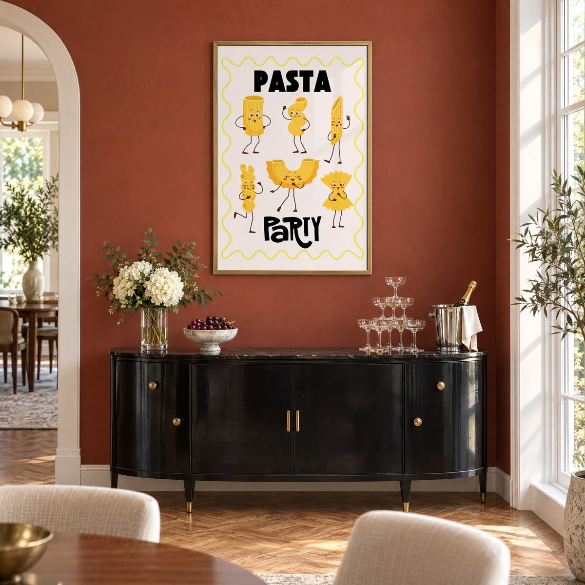 Pasta Party cartoon noodles print in a brass frame on a terracotta wall above a black buffet with a champagne tower