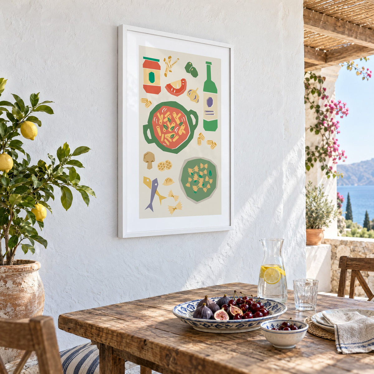 Penne pot and pesto farfalle cut-paper print in a white frame on a whitewashed terrace wall above a lunch table with figs and cherries, seen at an angle