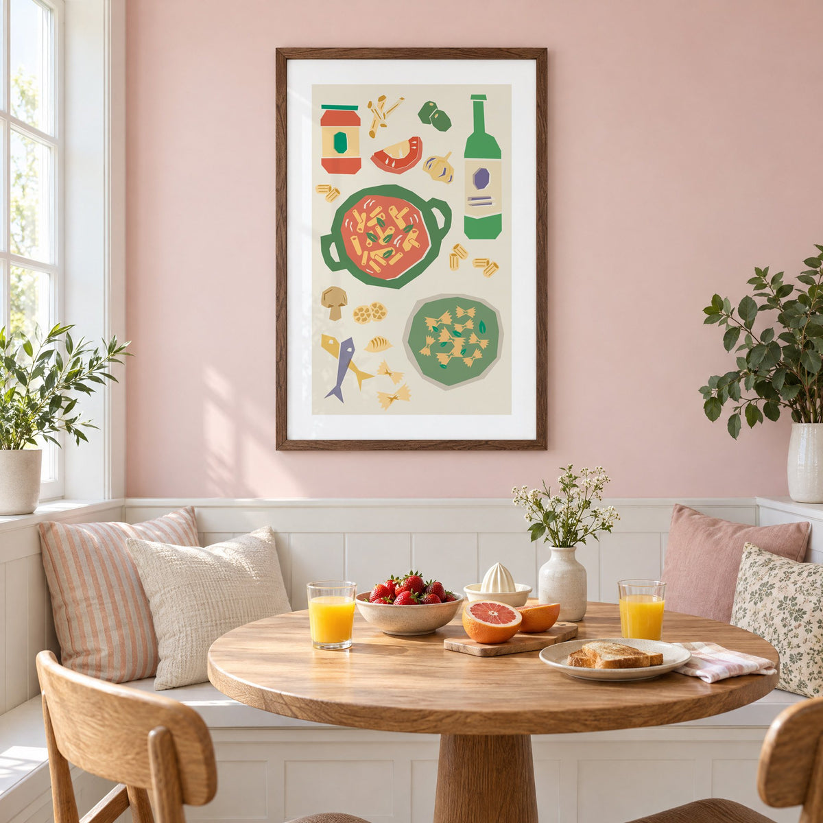 Penne pot and pesto farfalle cut-paper print in a walnut frame on a pastel pink wall above a breakfast nook with strawberries and orange juice