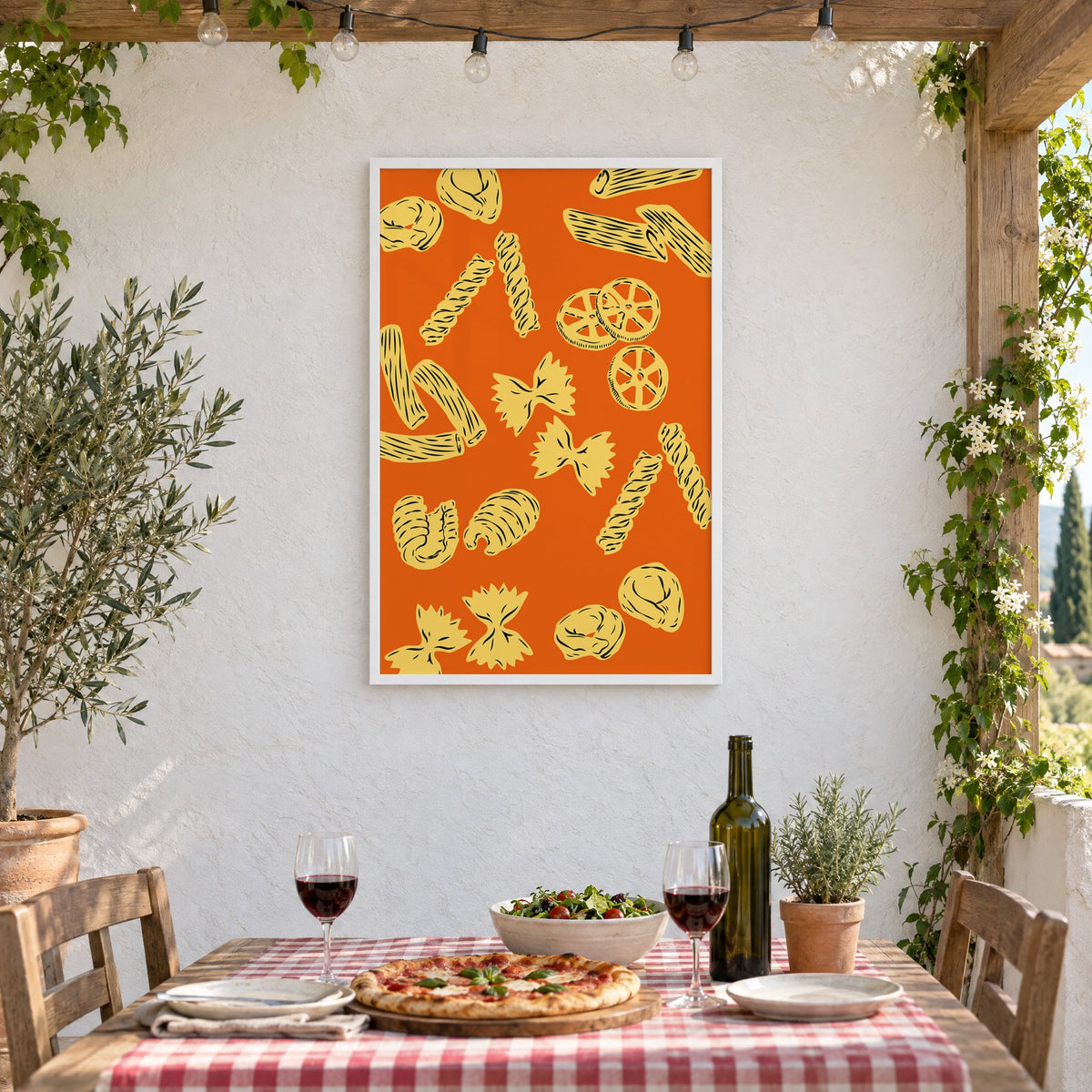 Orange pasta pattern woodcut-style print in a white frame on a stucco wall above a checked-cloth table with pizza and red wine