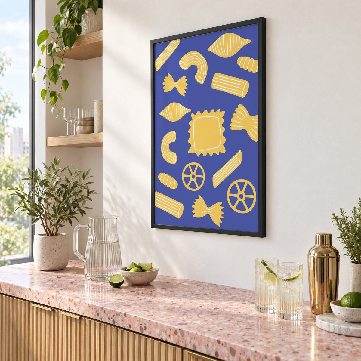 Yellow pasta shapes pattern on blue print in a black frame above a pink terrazzo cocktail counter with limes, seen at an angle