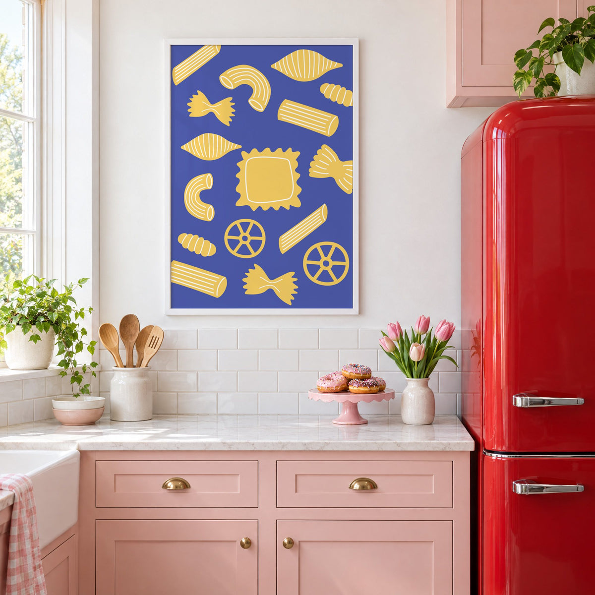 Yellow pasta shapes pattern on blue print in a white frame above pink cabinets beside a red retro fridge