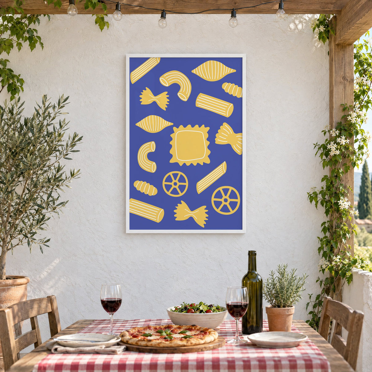 Yellow pasta shapes pattern on blue print in a white frame on a stucco wall above a checked-cloth table with pizza and red wine