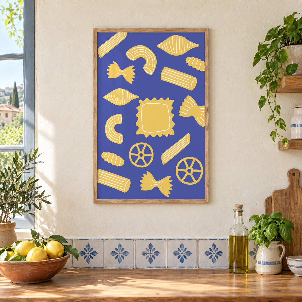 Yellow pasta shapes pattern on blue print in an oak frame on a cream plaster wall above a worktop with a bowl of lemons and blue-and-white tiles