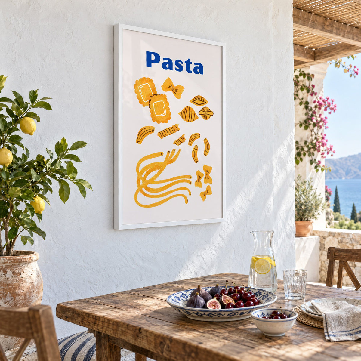 Pasta blue title watercolor pasta shapes print in a white frame on a whitewashed terrace wall above a lunch table with figs and cherries, seen at an angle