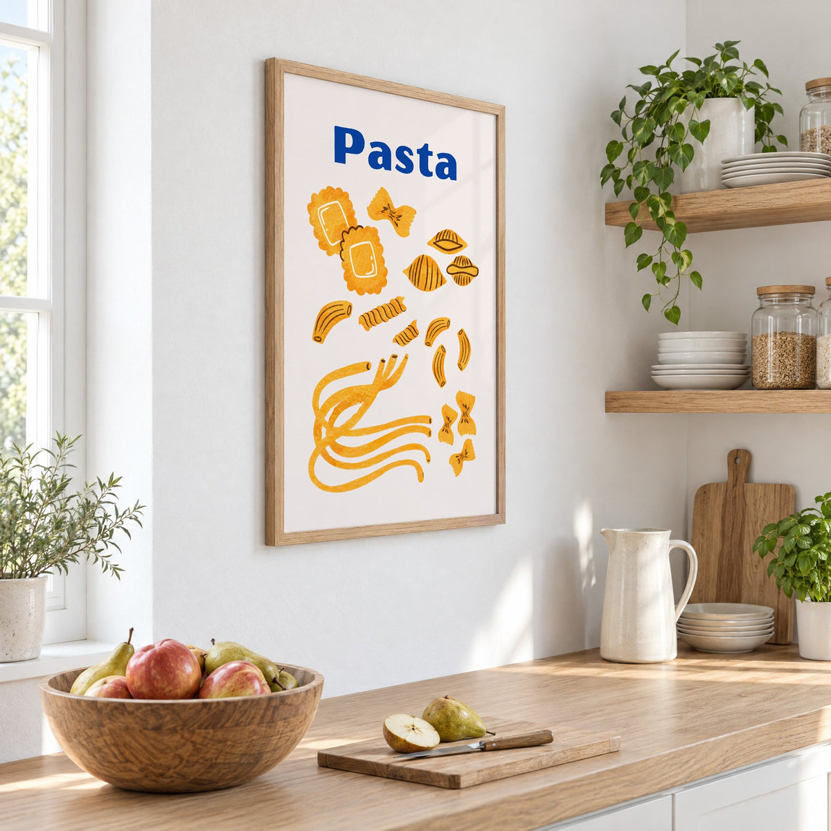 Pasta blue title watercolor pasta shapes print in an oak frame on a white kitchen wall above a counter with apples and pears, seen at an angle