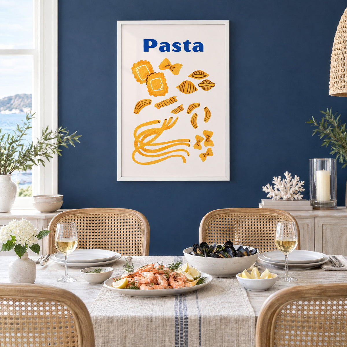 Pasta blue title watercolor pasta shapes print in a white frame on a navy wall above a dining table set with shrimp and mussels