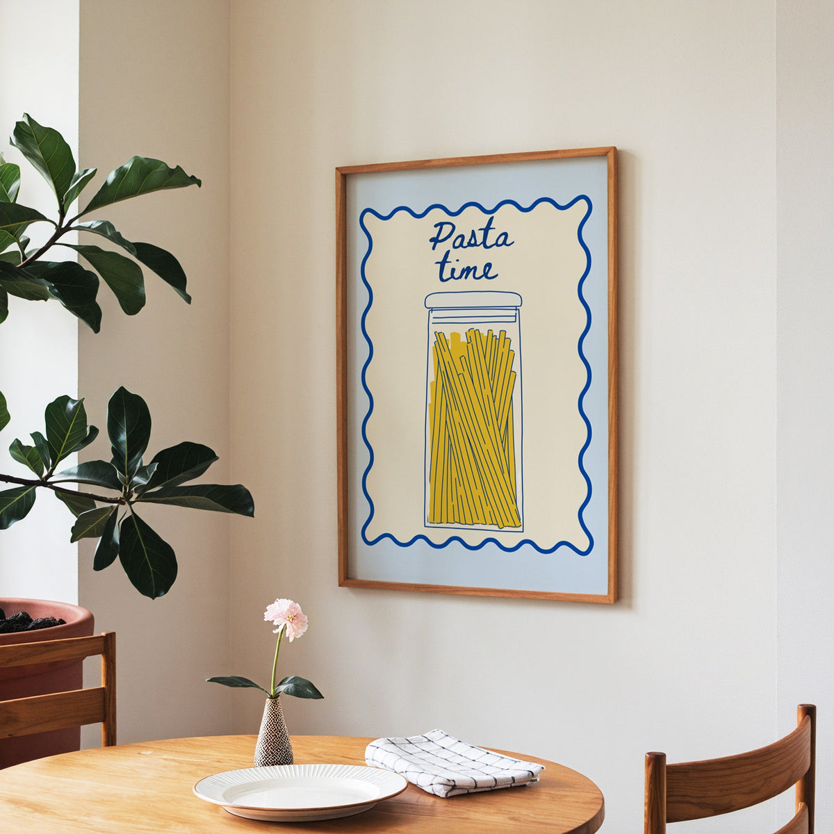 Pasta Time jar print in a walnut frame above a round table beside a fiddle-leaf fig