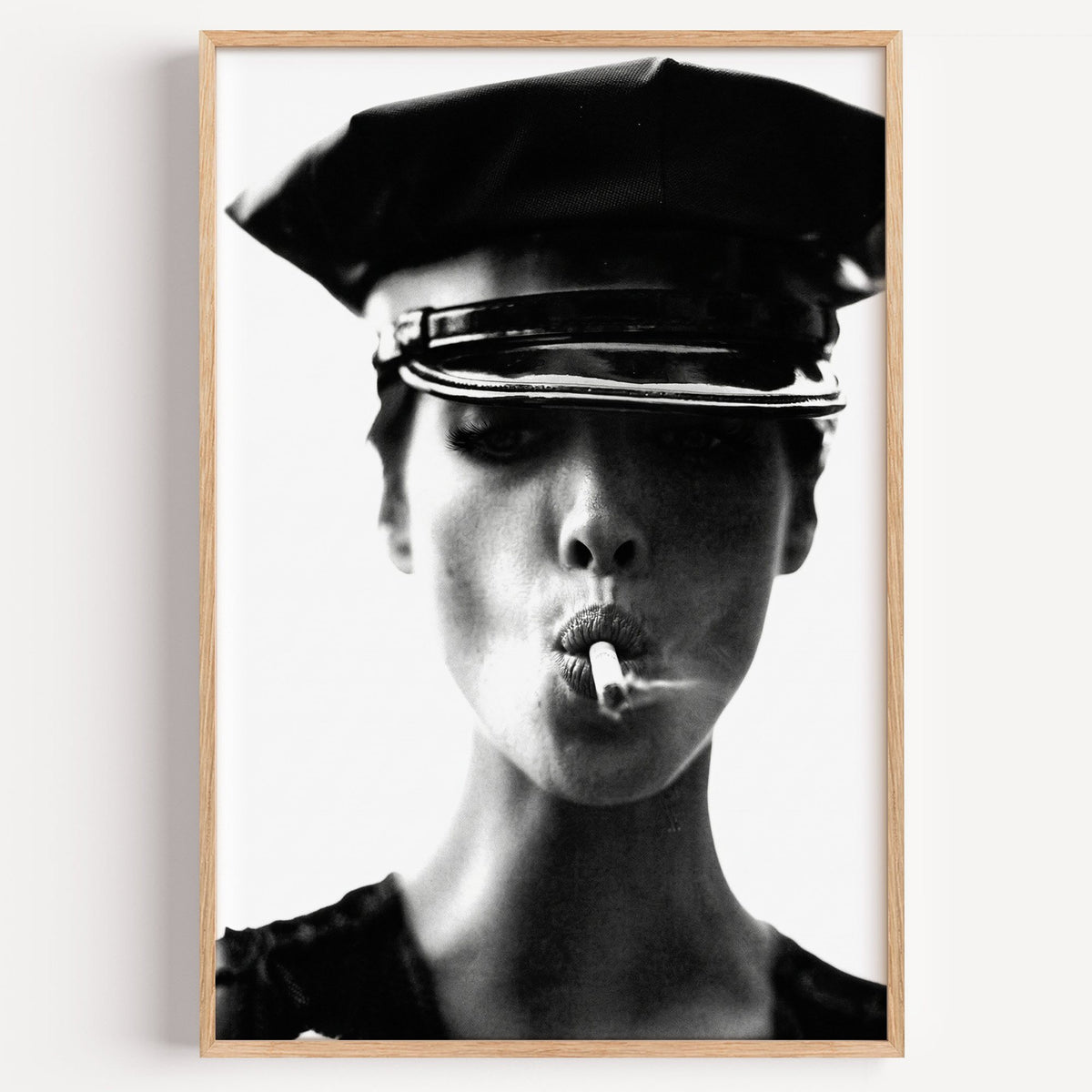 Close portrait under glossy leather cap print in a light oak frame on a plain white wall
