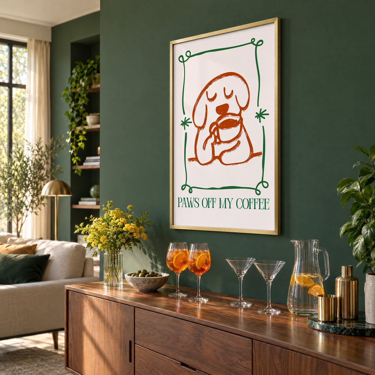 PAWS OFF MY COFFEE dog and mug print in a brass frame on a bottle green wall above a sideboard with spritz and martini glasses, seen at an angle