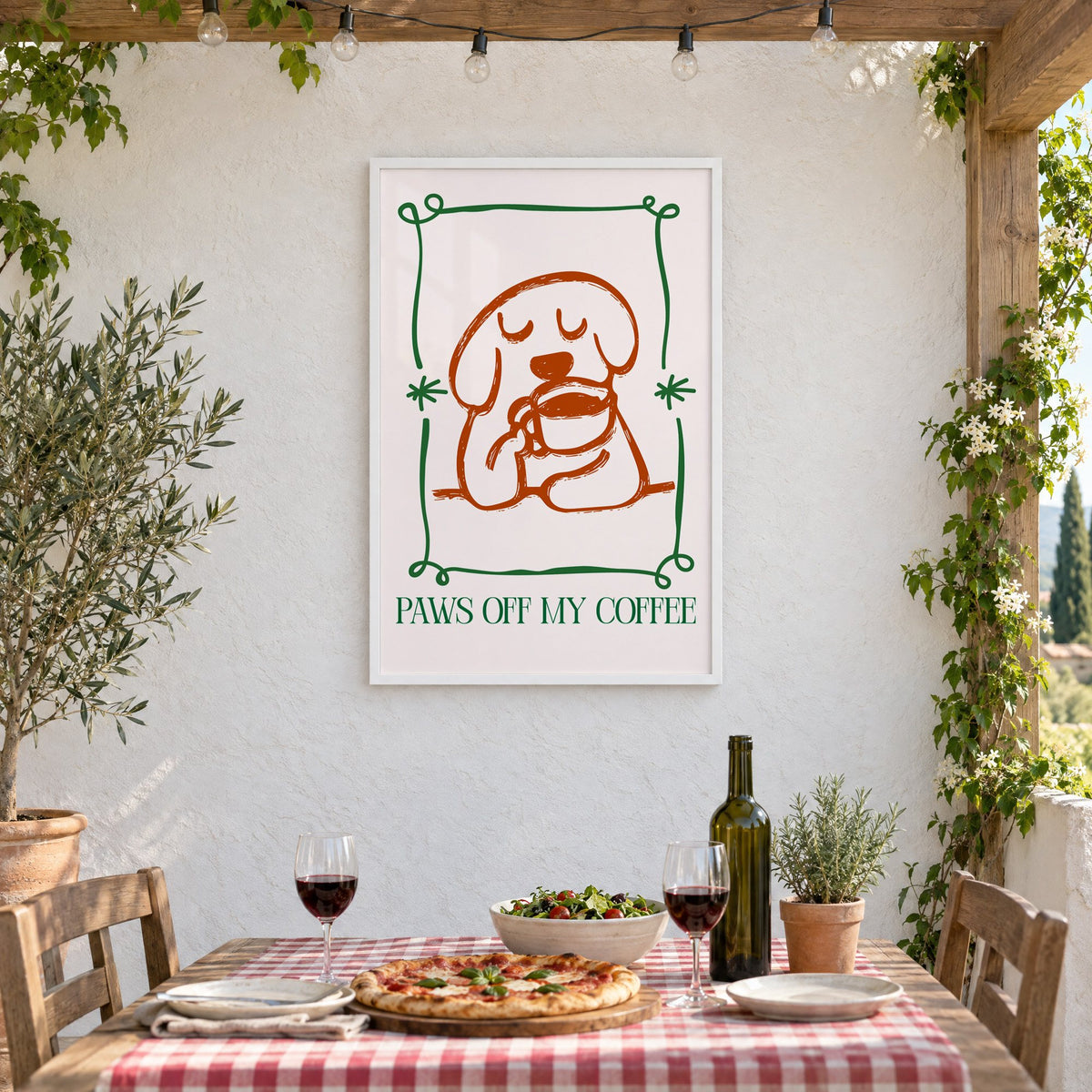 PAWS OFF MY COFFEE dog and mug print in a white frame on a stucco wall above a checked-cloth table with pizza and red wine
