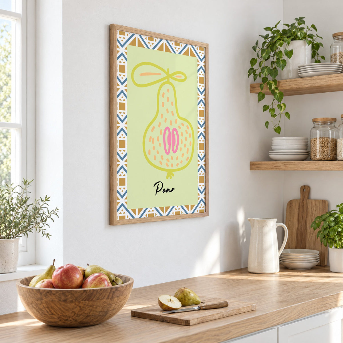 Pear lime line-art zigzag border print in an oak frame on a white kitchen wall above a counter with apples and pears, seen at an angle