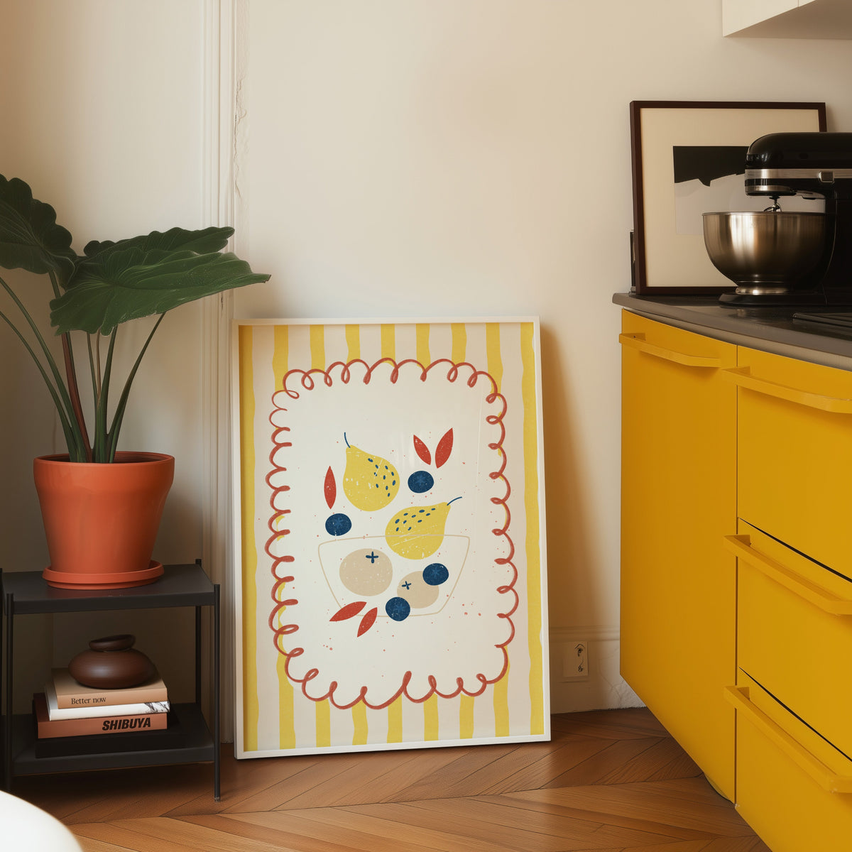Pears and blueberries print in a white frame on parquet beside a yellow kitchen