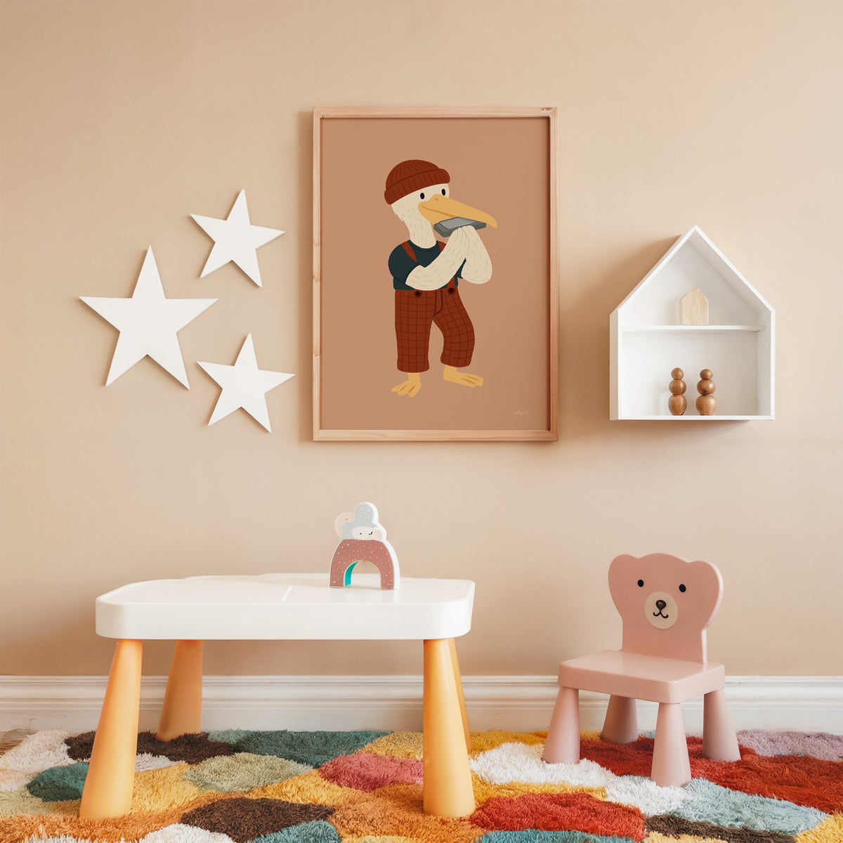 Pelican with harmonica and beanie nursery print in an oak frame on a peach wall above a kids table with wall stars