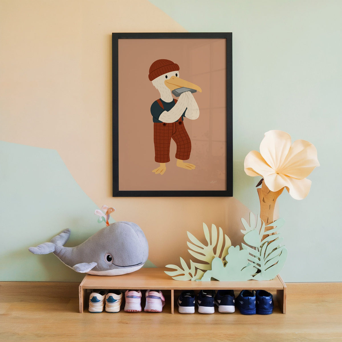 Pelican with harmonica and beanie nursery print in a black frame on a mint and peach wall above a whale plush