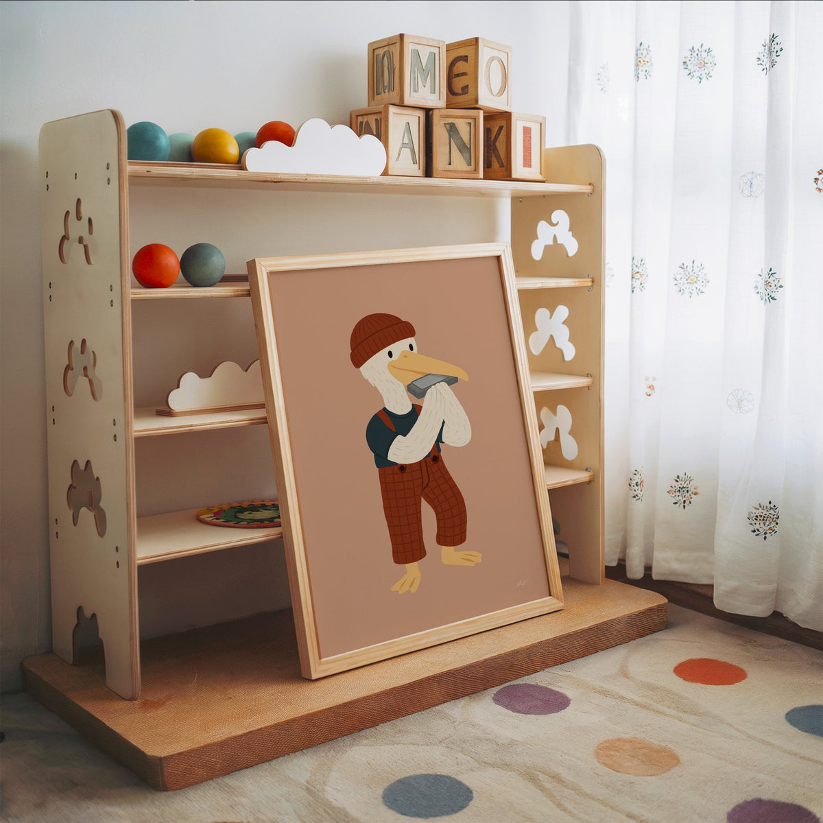 Pelican with harmonica and beanie nursery print in an oak frame leaning on a toy shelf with wooden letter blocks
