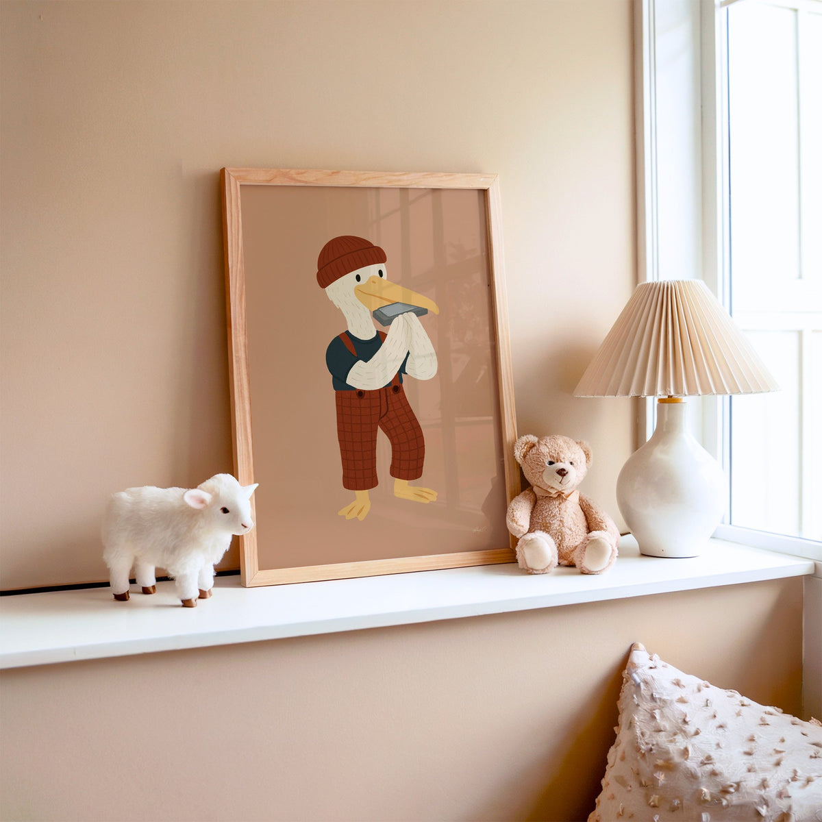 Pelican with harmonica and beanie nursery print in an oak frame on a window ledge with a toy lamb and teddy