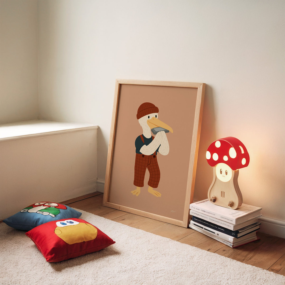 Pelican with harmonica and beanie nursery print in an oak frame leaning on a rug beside a mushroom lamp and floor cushions