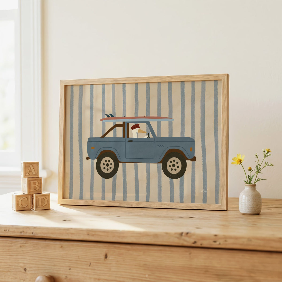Pelican driving blue surf truck nursery print in an oak frame on a wooden dresser beside ABC blocks
