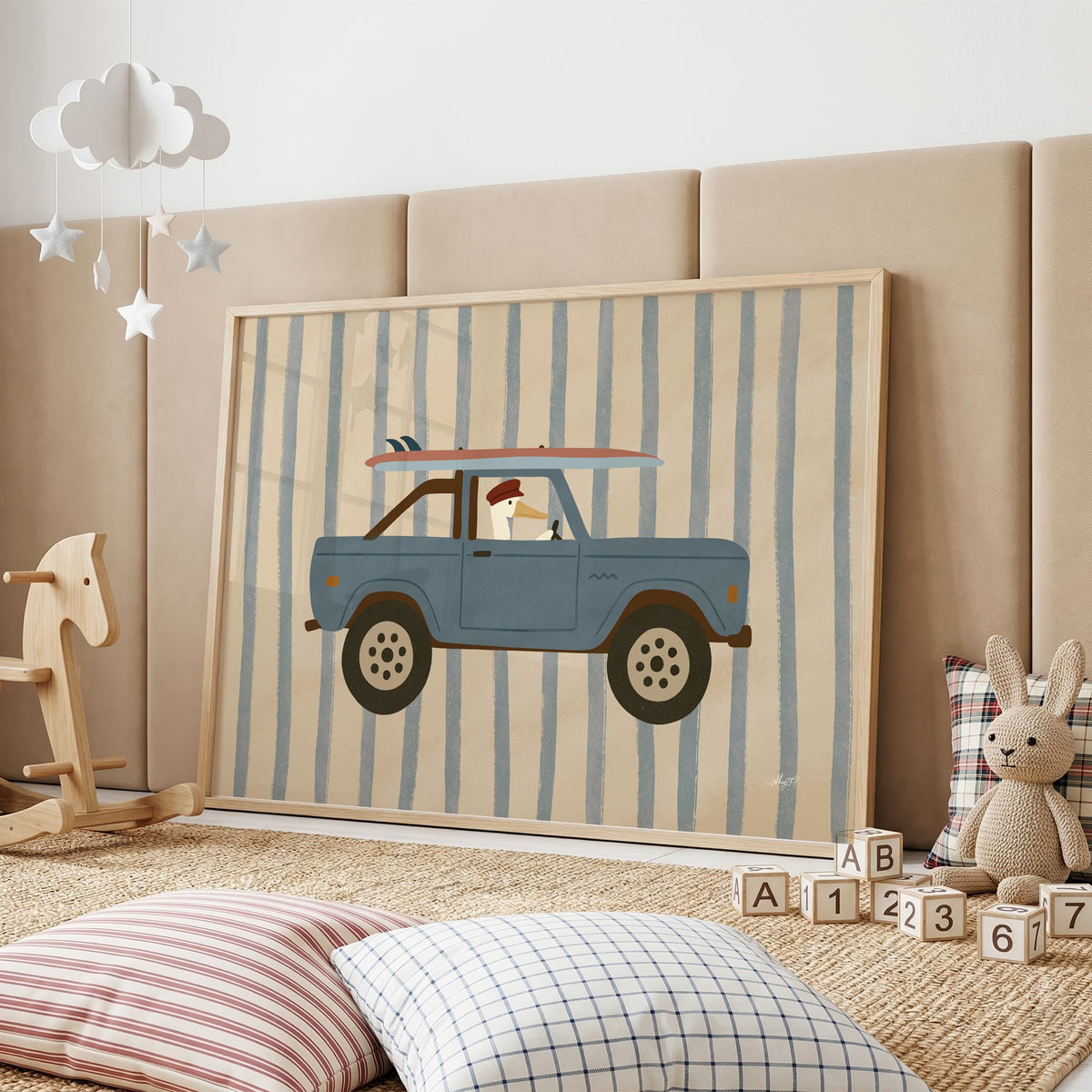 Pelican driving blue surf truck nursery print in an oak frame on a padded wall by a wooden rocking horse