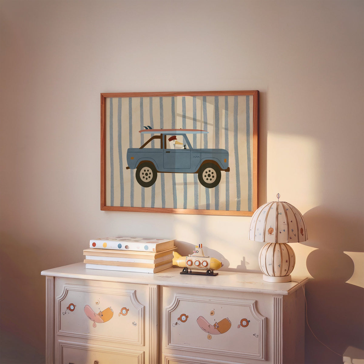 Pelican driving blue surf truck nursery print in a cherry wood frame above a painted dresser and lamp