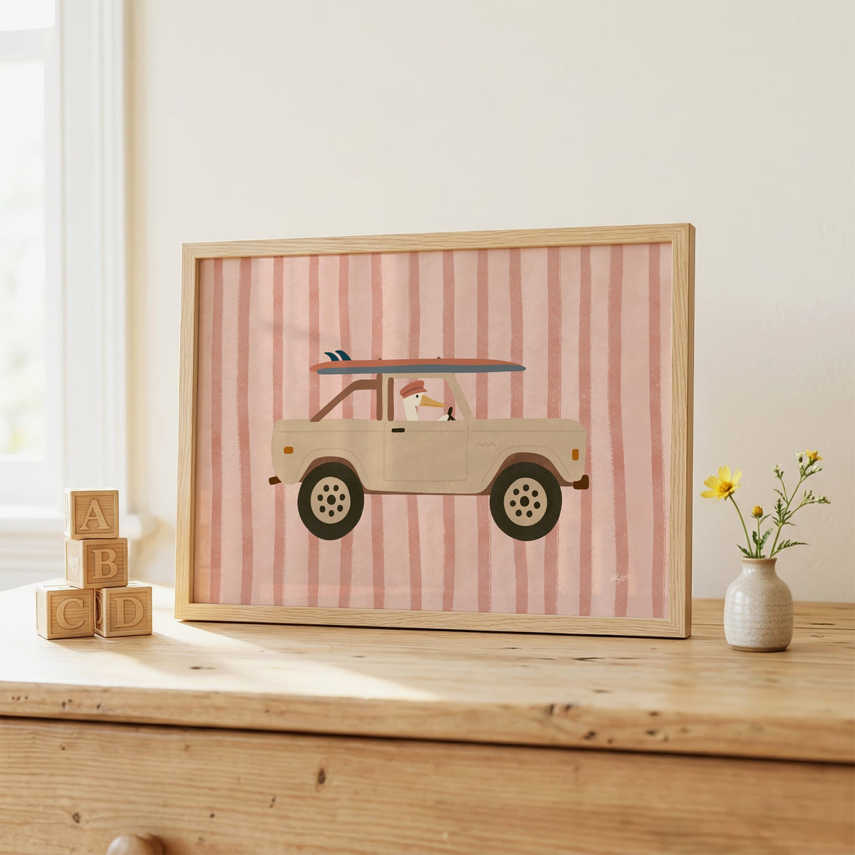 Pelican driving beige truck pink nursery print in an oak frame on a wooden dresser beside ABC blocks