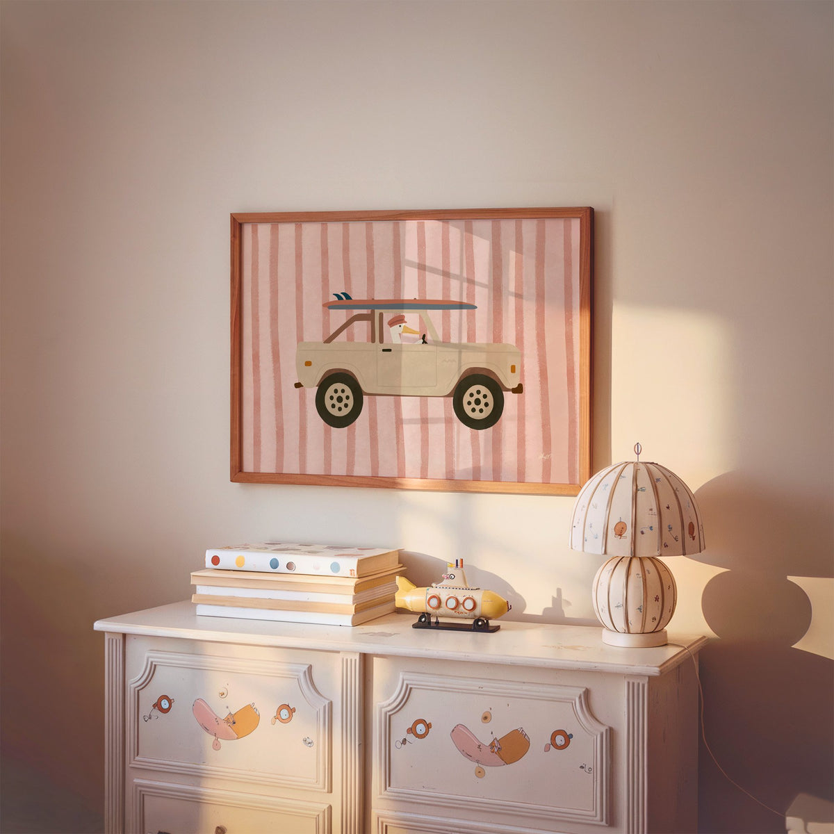 Pelican driving beige truck pink nursery print in a cherry wood frame above a painted dresser and lamp