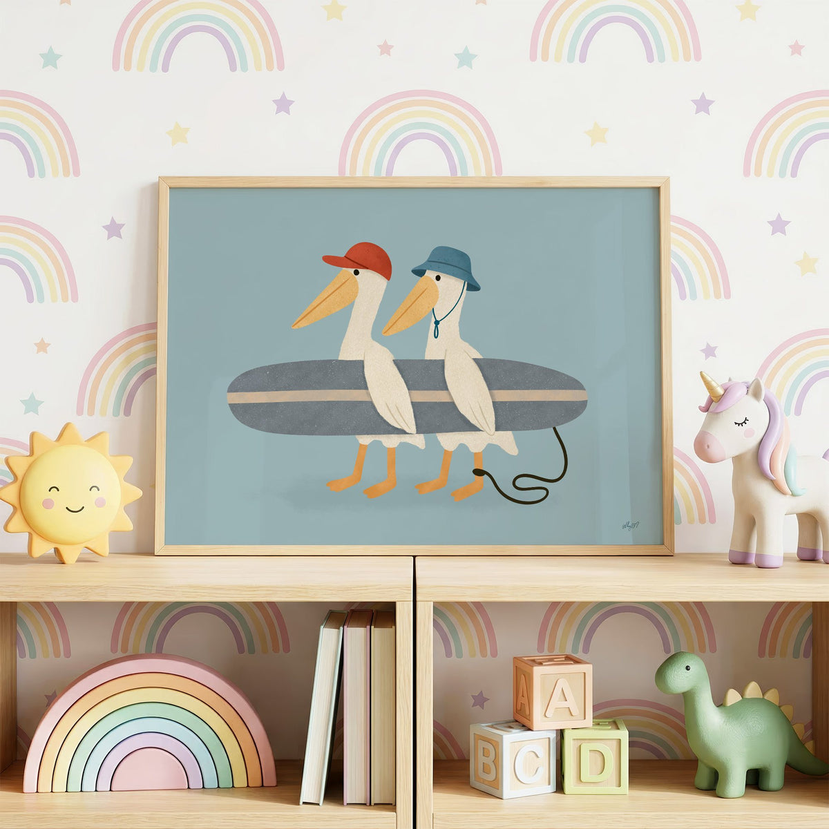 Two pelicans carrying surfboard nursery print in an oak frame on a toy shelf against rainbow wallpaper
