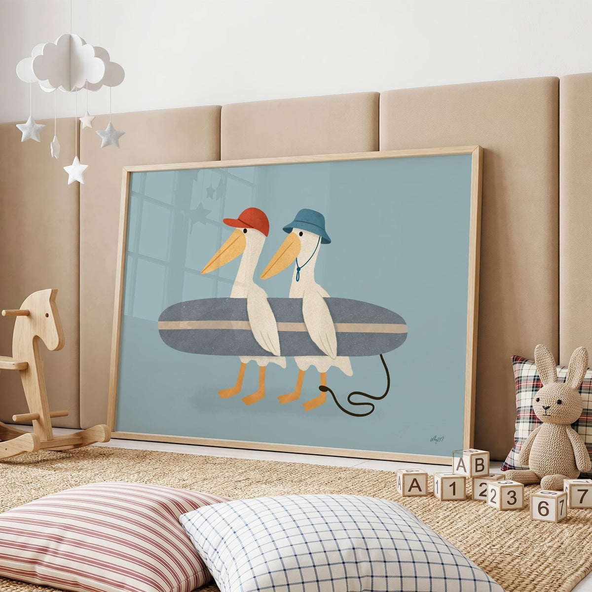 Two pelicans carrying surfboard nursery print in an oak frame on a padded wall by a wooden rocking horse