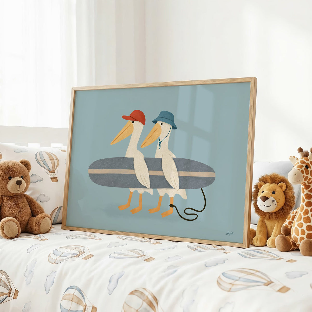 Two pelicans carrying surfboard nursery print in an oak frame on a kids bed with hot air balloon bedding